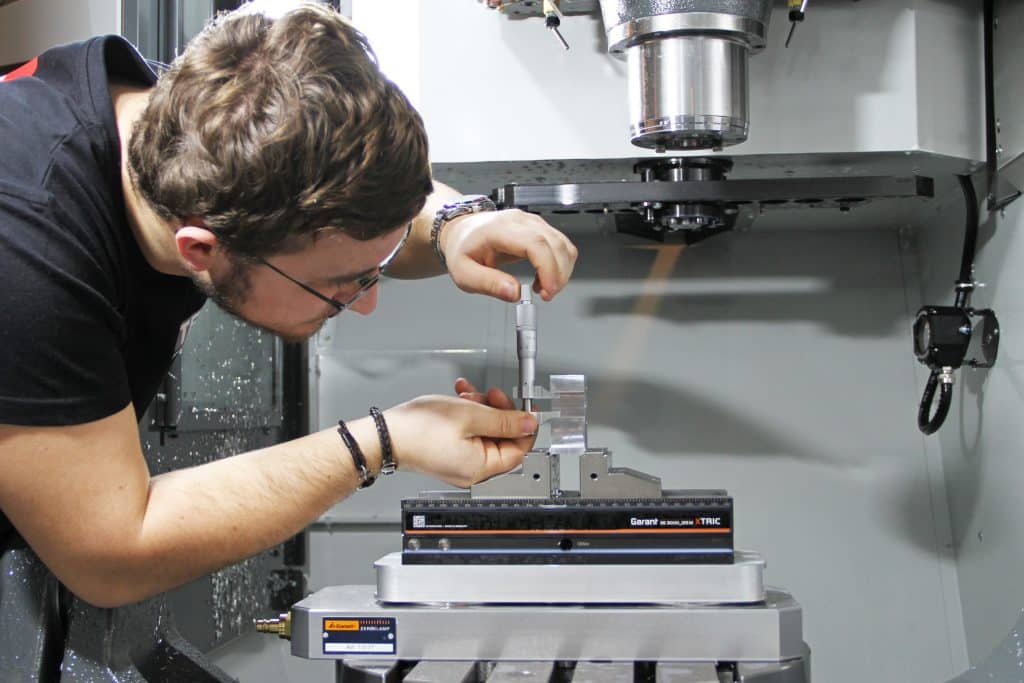 Étudiant en train de mesurer une pièce métallique dans une machine à commande numérique HAAS.