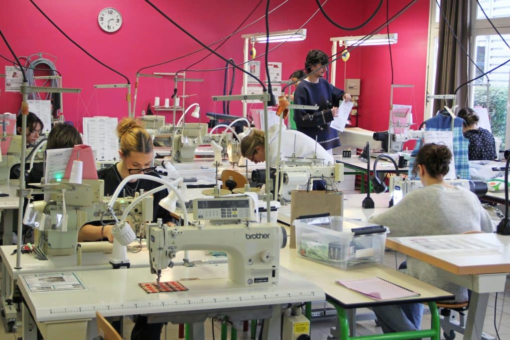 Atelier de couture avec des élèves en train d'apprendre à coudre sur plusieurs machines.