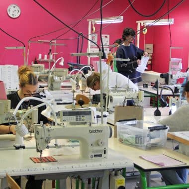 Atelier de couture avec des élèves en train d'apprendre à coudre sur plusieurs machines.