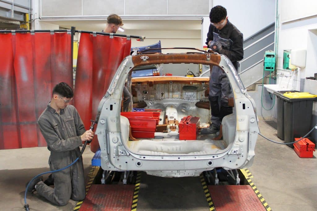 Lycéens en train de réparer la carrosserie d'une voiture dans un atelier de la Joliverie.