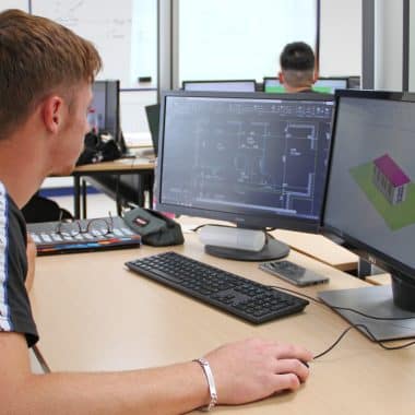 Étudiant devant son ordinateur en train de dessiner des plans d'architecture d'un bâtiment.