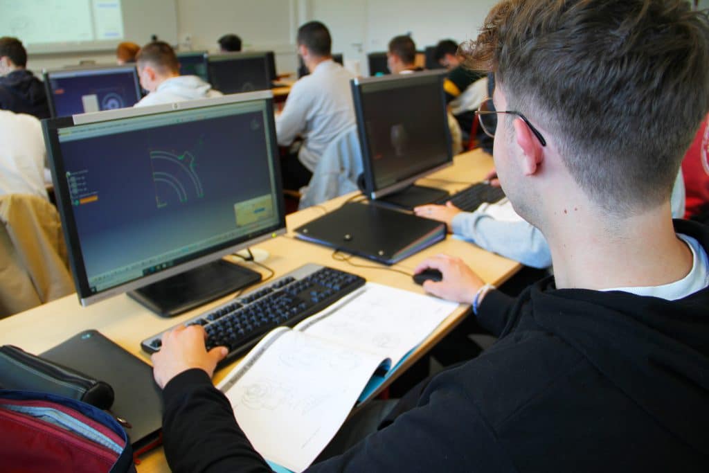 Étudiant devant son écran d'ordinateur en train de dessiner des pièces industrielles.