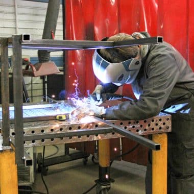 Élève en train de souder une pièce métallique dans un atelier.