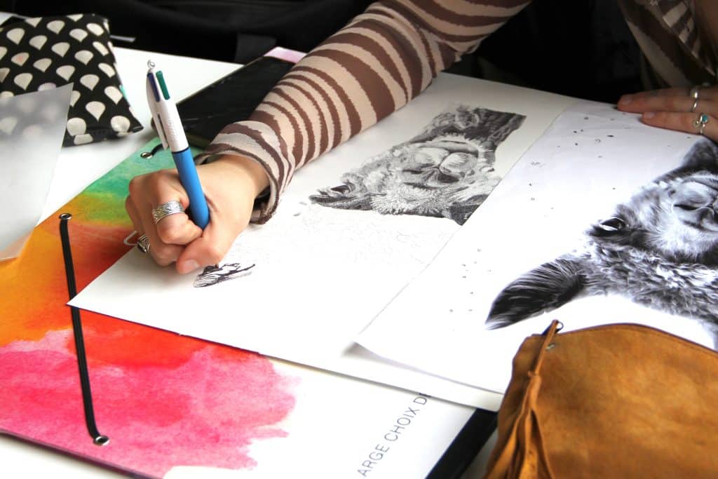Élève en train de dessiner sur une feuille avec ses crayons.