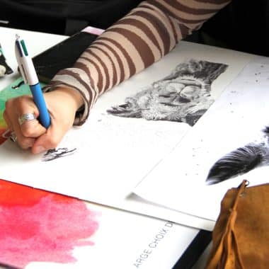 Élève en train de dessiner sur une feuille avec ses crayons.