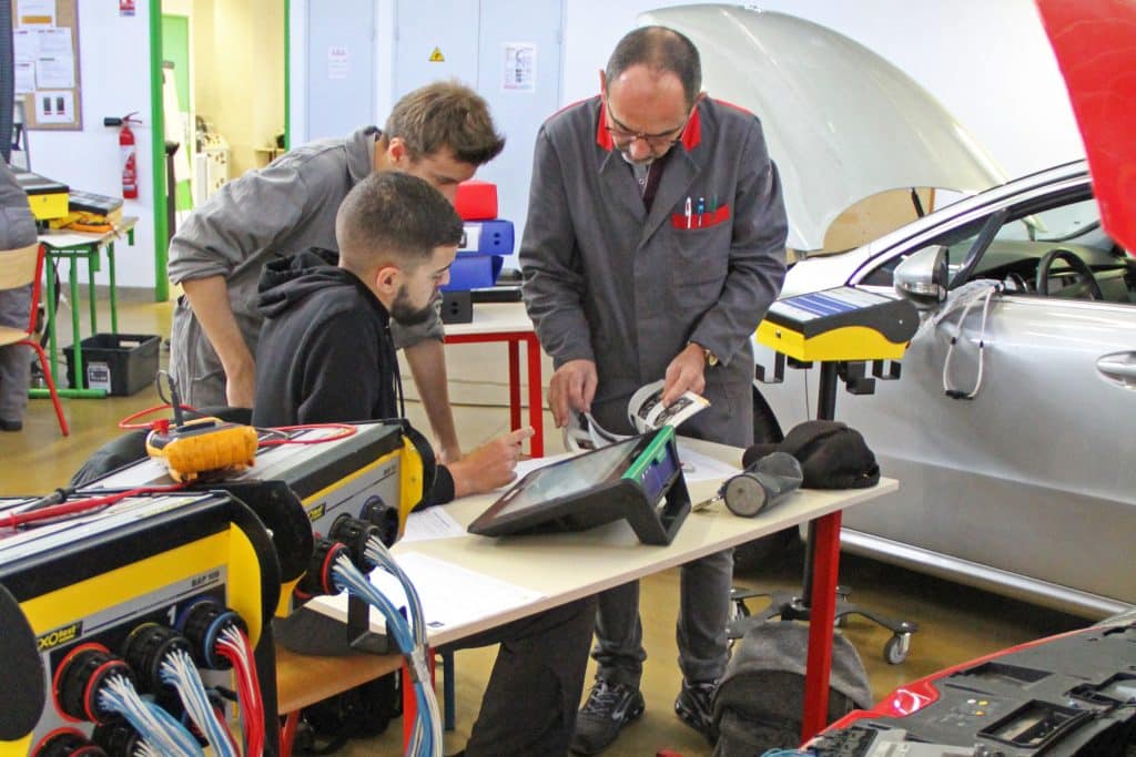2 étudiants et leur professeur en train d'analyser un véhicule pour en faire la maintenance.