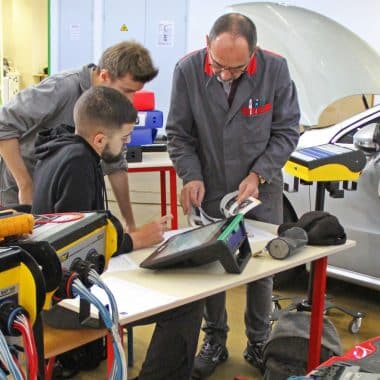 2 étudiants et leur professeur en train d'analyser un véhicule pour en faire la maintenance.
