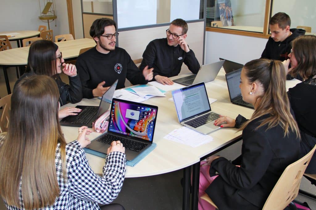 Étudiants et étudiantes, devant leurs ordinateurs portables, autour d'une table, en train de discuter.