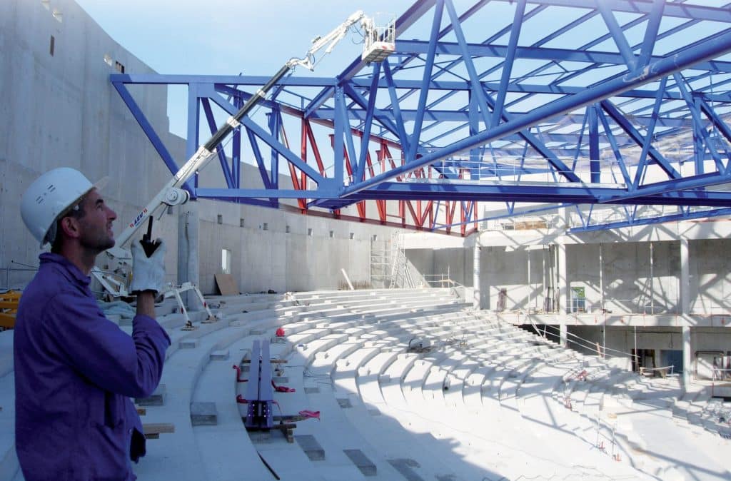 Chantier d'un bâtiment avec une structure métallique bleue et un homme qui parle au talkie walkie.