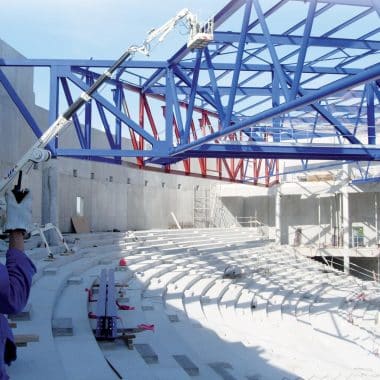 Chantier d'un bâtiment avec une structure métallique bleue et un homme qui parle au talkie walkie.
