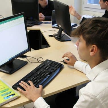 Jeune qui travaille sur un tableau Excel devant son écran d'ordinateur en salle informatique.