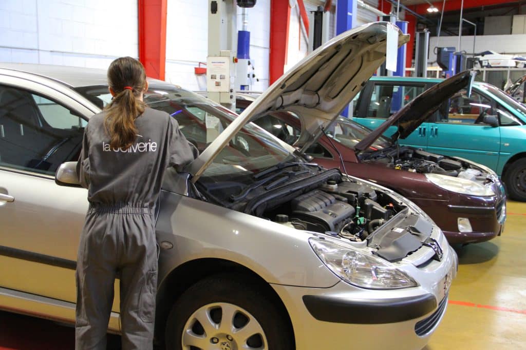 Fille lycéenne en train de réparer une voiture dans un atelier automobile.