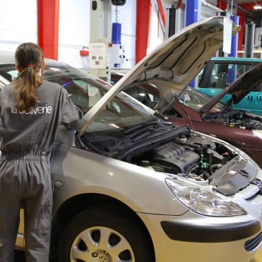 Fille lycéenne en train de réparer une voiture dans un atelier automobile.