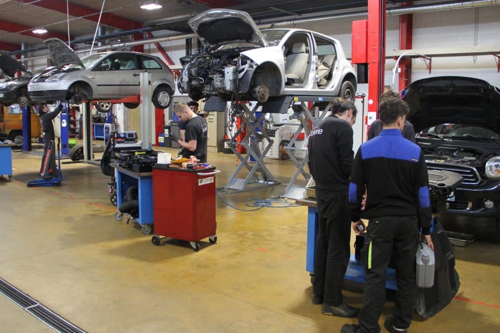 Plusieurs élèves de bac professionnel avec leur professeur en train de réparer des voitures dans le pôle automobile de la joliverie