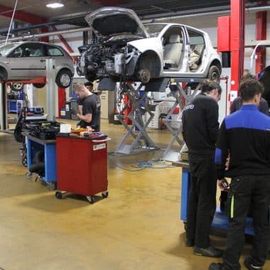 Plusieurs élèves de bac professionnel avec leur professeur en train de réparer des voitures dans le pôle automobile de la joliverie