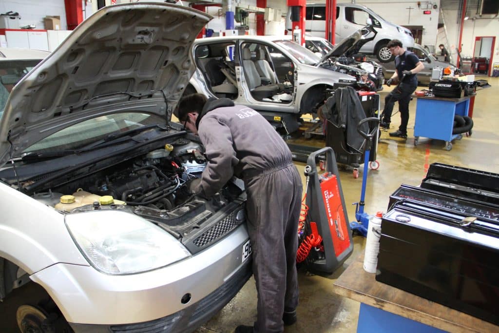 Lycéen en pleine réparation sous le capot d'une voiture.