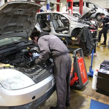 Lycéen en pleine réparation sous le capot d'une voiture.