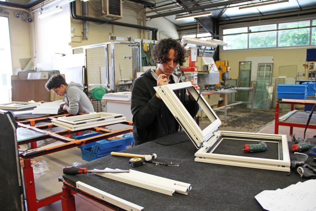 Lycéen en menuiserie aluminium et verre en train de travailler sur une fenêtre dans un atelier.