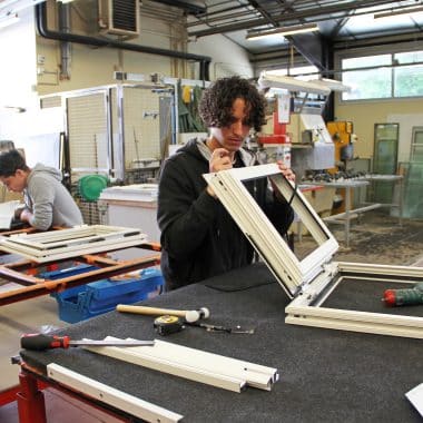 Lycéen en menuiserie aluminium et verre en train de travailler sur une fenêtre dans un atelier.