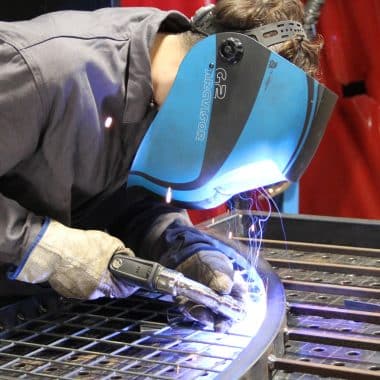 Un lycéen en train de réaliser une soudure avec un casque devant le visage.