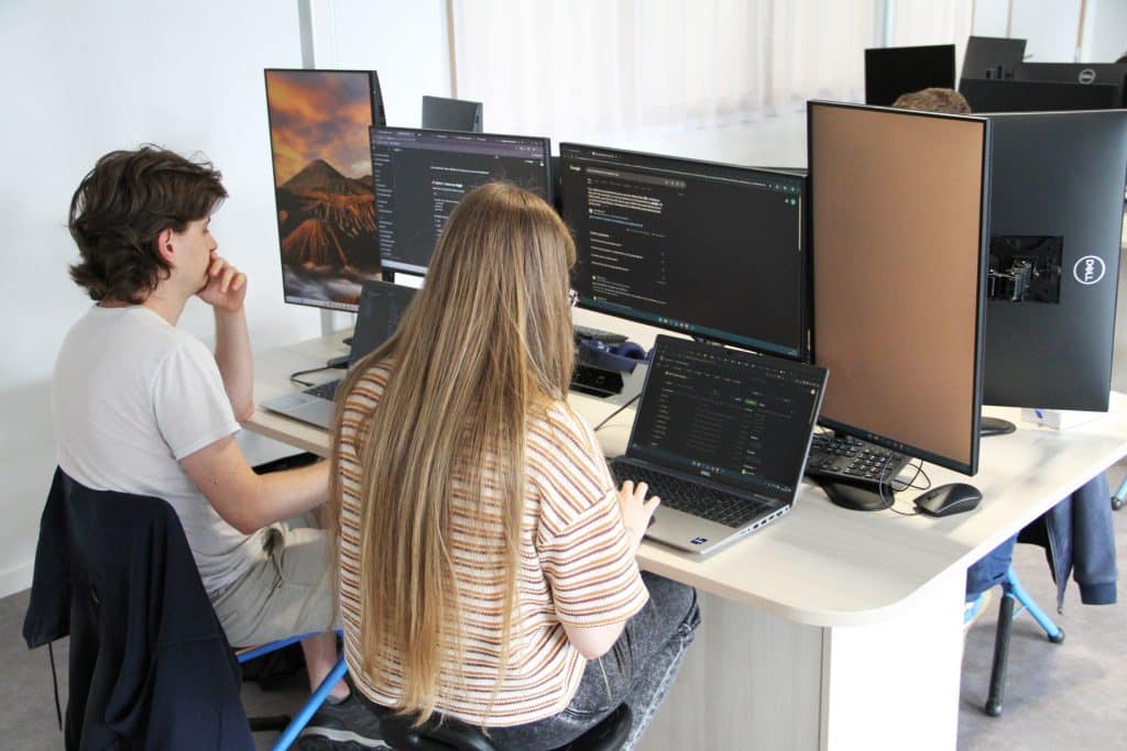 2 étudiants qui travaillent devant plusieurs écran dans une salle informatique de la Joliverie.